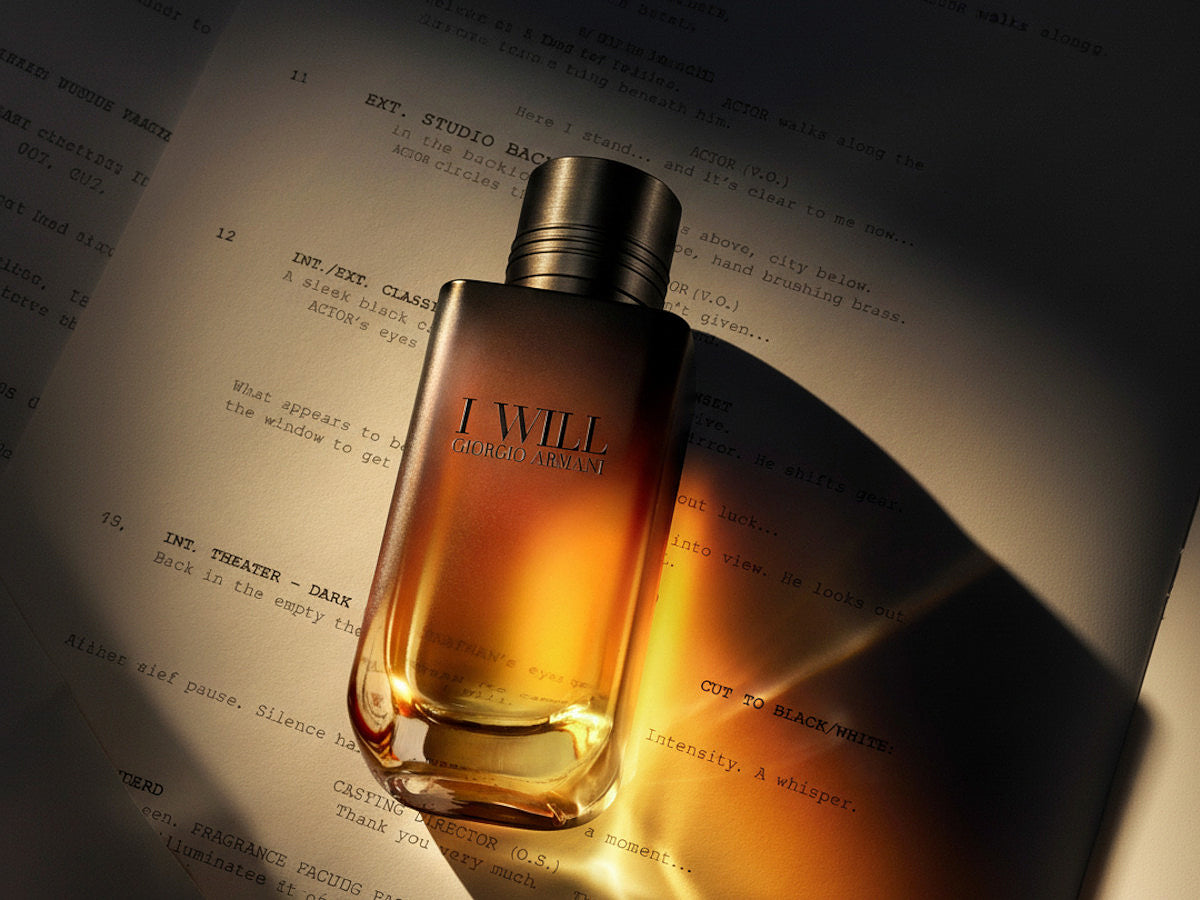 Giorgio Armani I Will eau de parfum in an amber gradient glass bottle with a dark cap, lying on the pages of a film script lit by a dramatic beam of warm light