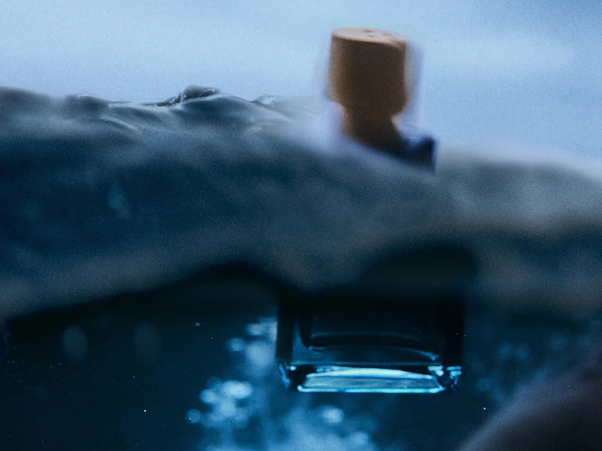 Goldfield & Banks Pacific Rock Swell extrait de parfum, a square glass bottle with a wooden cap, partly submerged in rippling deep blue ocean water