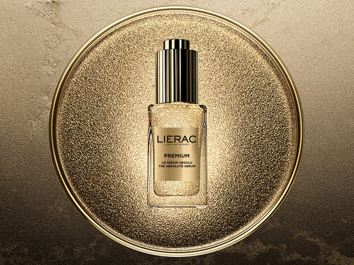 Lierac Premium The Absolute Serum in a gold glitter bottle with a gold cap, centred on a textured gold disc against a gold and black marbled background