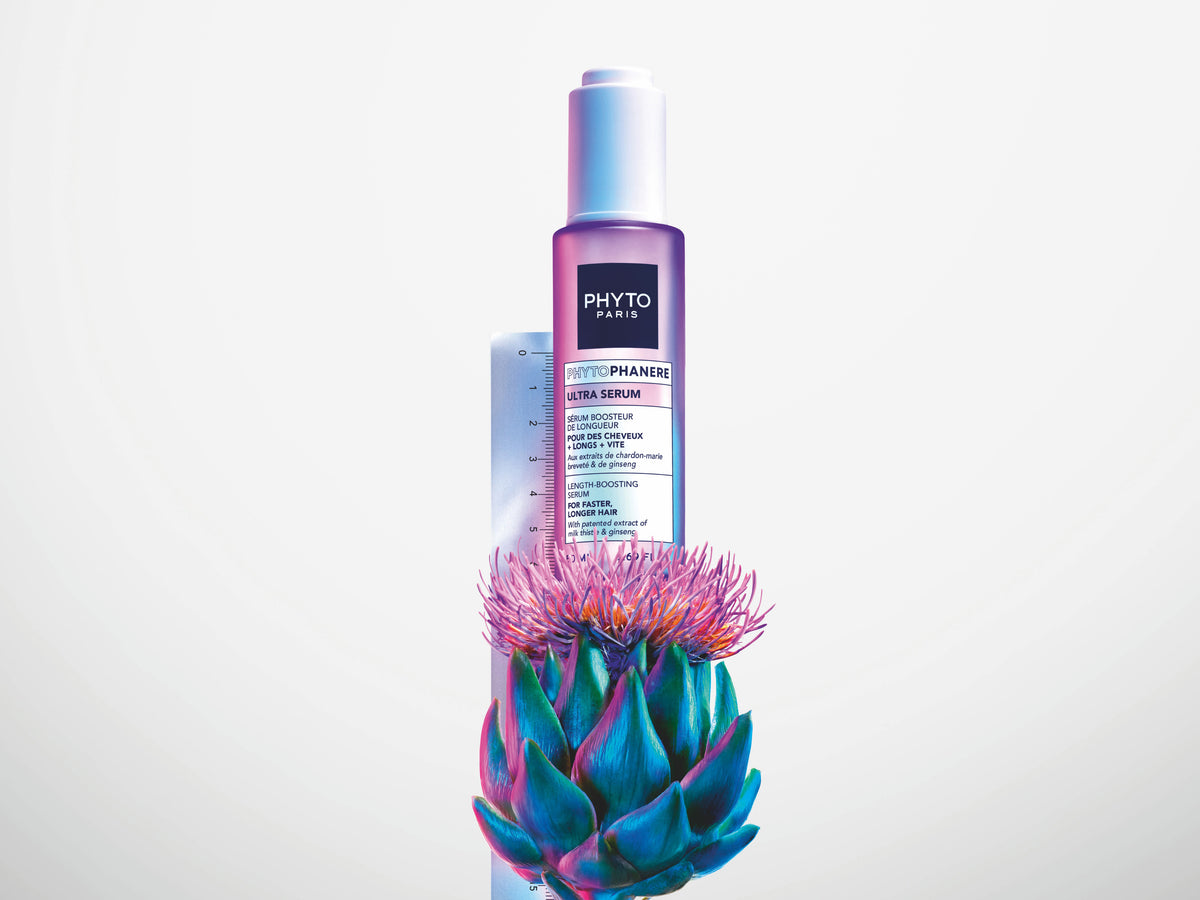 Phyto Phytophanere Ultra Serum in a lilac to blue gradient pump bottle rising from a vivid blue and pink artichoke flower, on a white background