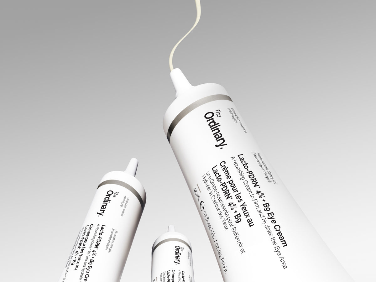 Three white cosmetic tubes of The Ordinary Lactate-Myo Cream arranged diagonally on a light gray gradient background, with one tube open and showing a thin cream line.